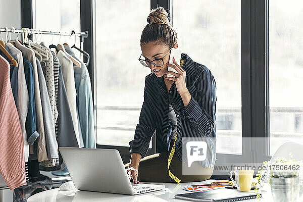 Smiling businesswoman using laptop and talking on mobile phone in office