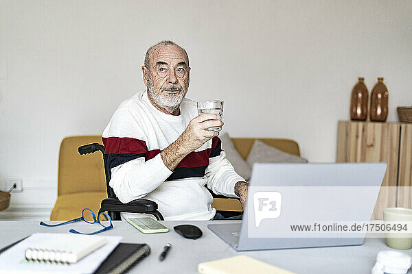 Disabled businessman holding drinking glass at home