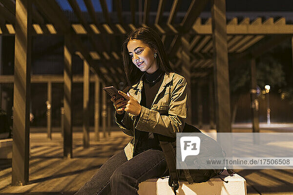 Woman with backpack using smart phone on bench