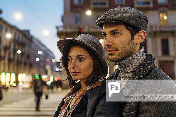 Confident young couple wearing hat looking away in city