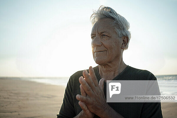 Smiling senior man with hands clasped at beach