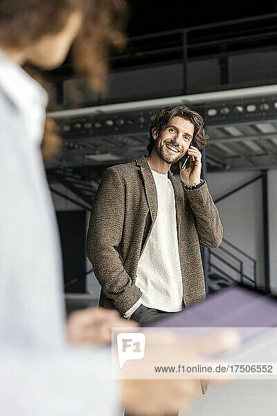 Lächelnder Geschäftsmann mit der Hand in der Tasche  der mit dem Mobiltelefon spricht