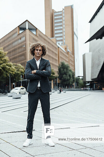 Confident businessman with arms crossed standing at city square