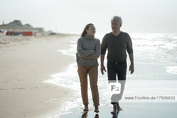 Tochter mit verschränkten Armen geht mit Vater am Strand spazieren