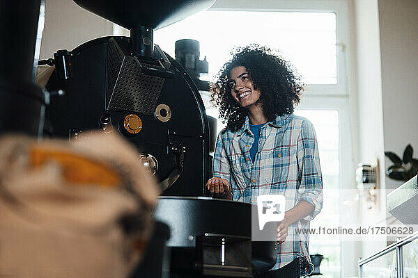 Smiling owner standing near machine in coffee roastery