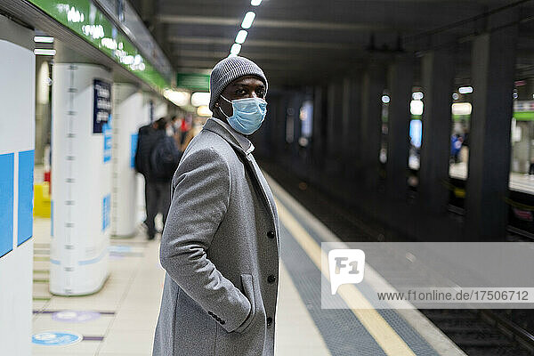 Businessman with hand in pocket wearing protective face mask standing at railroad station