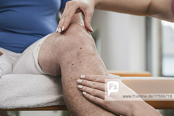 Junge Physiotherapeutin massiert zu Hause das Knie eines behinderten Patienten
