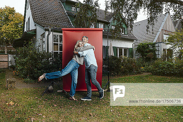 Couple hugging each other in front of red backdrop at backyard