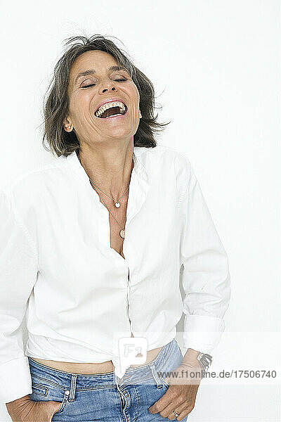 Frau mit geschlossenen Augen lacht vor weißem Hintergrund