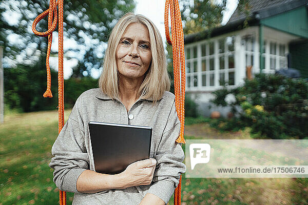 Blond woman with tablet PC on swing at backyard