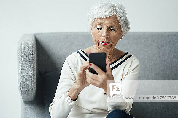 Ältere Frau benutzt Mobiltelefon auf Sofa