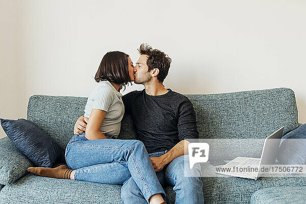 Zärtliches junges Paar küsst sich mit geschlossenen Augen zu Hause auf dem Sofa