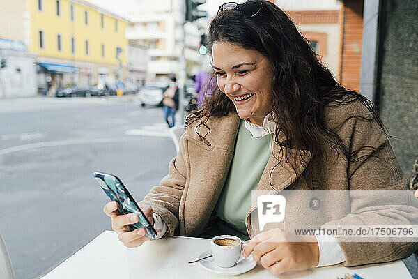 Glückliche Frau benutzt Smartphone  während sie im Straßencafé Kaffee trinkt