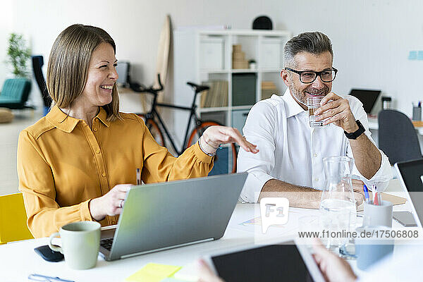 Smiling businesswoman gesturing with colleague drinking water at office