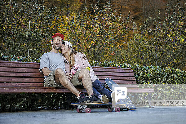 Couple with skateboards embracing each other sitting on bench by plants