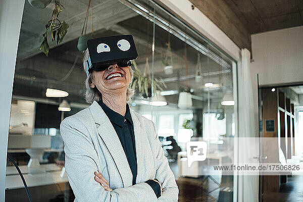 Smiling businesswoman with arms crossed using virtual reality headset in office