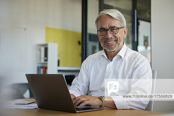 Smiling businessman working on laptop at workplace