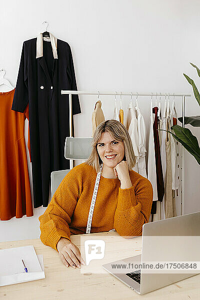 Young businesswoman with hand on chin sitting at desk in creative office