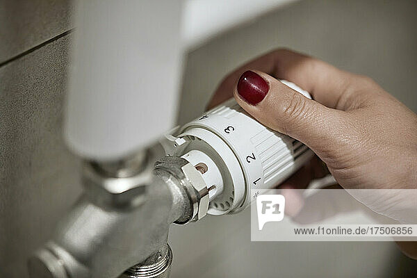 Woman adjusting thermostatic radiator valve of heating boiler at home