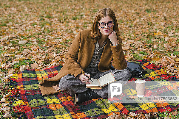 Smiling young woman sitting cross-legged on blanket in park