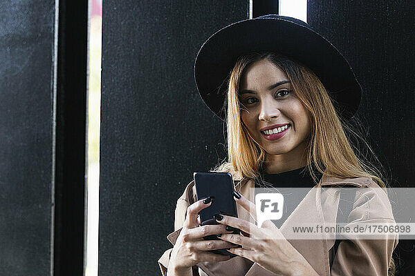 Woman holding mobile phone in front of black wall