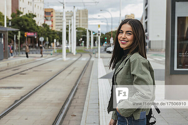 Smiling woman with hand in pocket at tram station