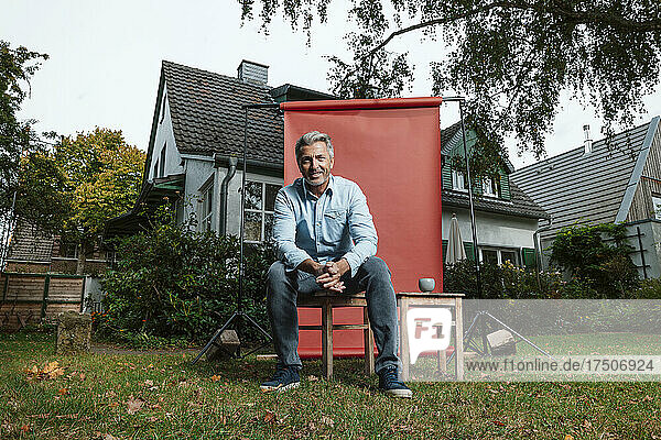 Smiling man sitting on stool at backyard