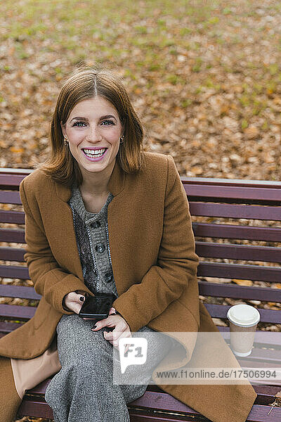 Happy woman with smart phone on park bench