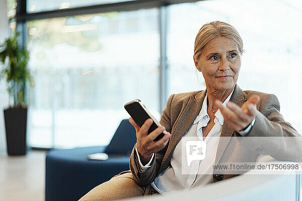 Businesswoman with mobile phone gesturing on sofa