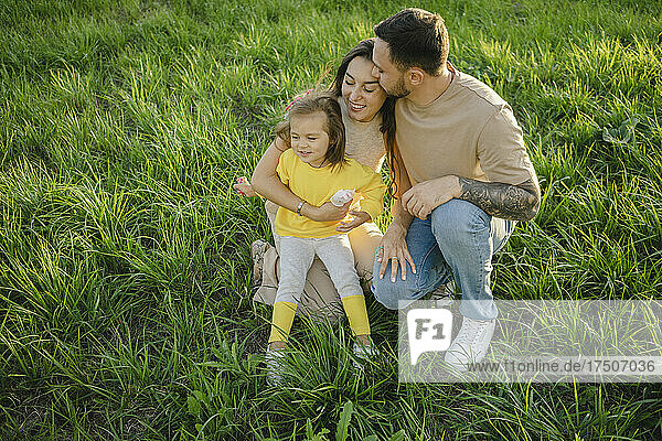 Man kissing woman holding daughter on grass