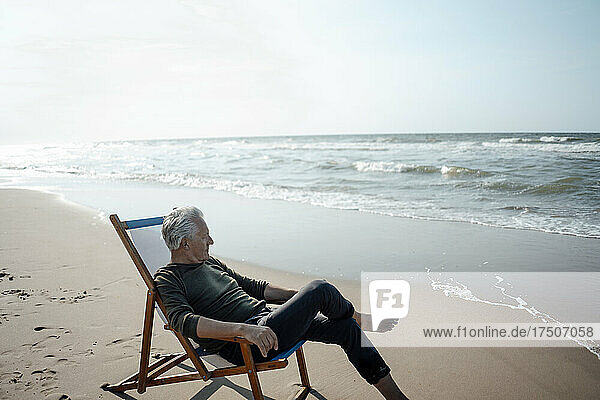 Senior man sitting on chair by seashore at beach