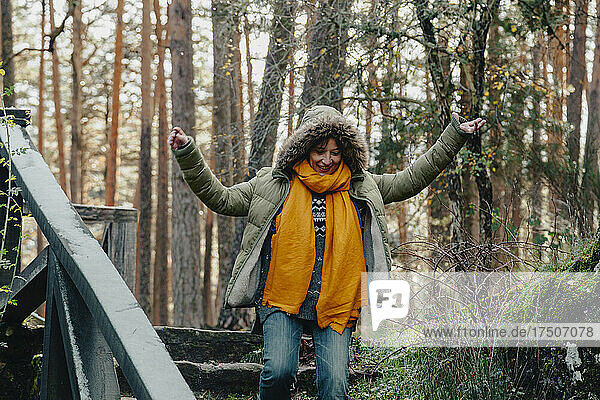 Happy woman with arms outstretched moving down on steps in forest
