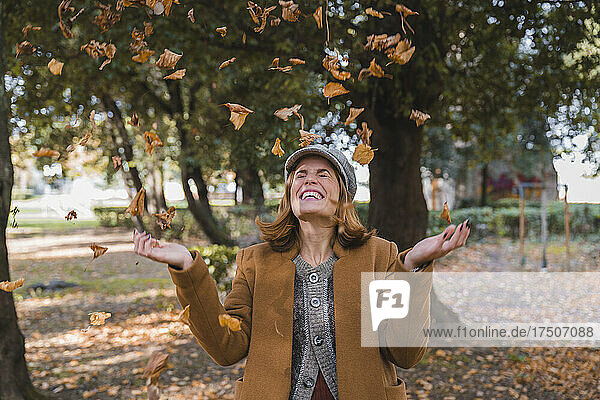 Cheerful woman throwing autumn leaves in air