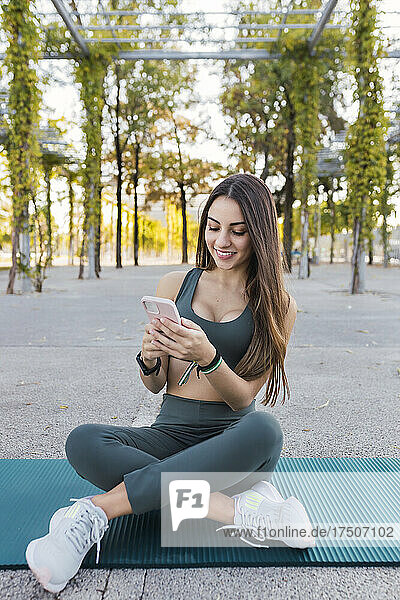 Smiling athlete using mobile phone on exercise mat