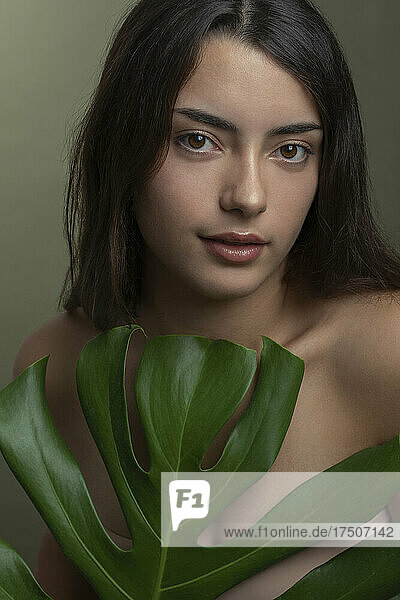 Young shirtless woman with green monstera leaf