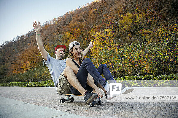 Playful couple skateboarding together on footpath