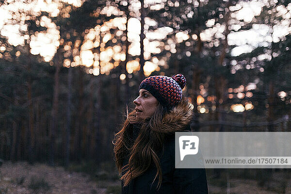 Woman wearing knit hat in forest at sunset