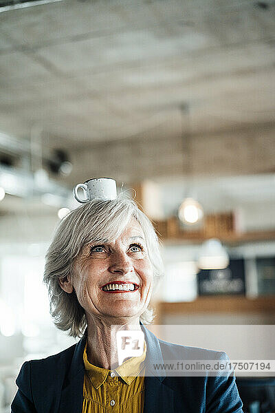 Happy senior businesswoman with cup on head in office