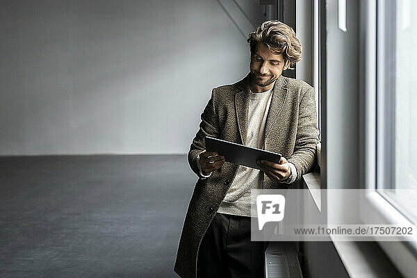 Businessman with tablet pc leaning on window