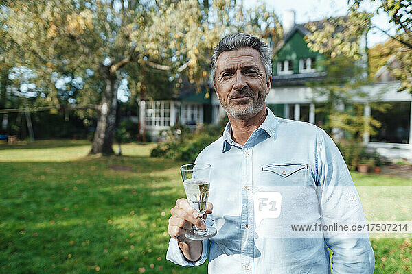 Smiling man holding champagne flute at backyard
