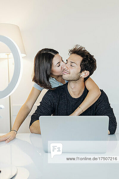 Junge Frau küsst ihren Freund  während sie im Heimbüro arbeitet