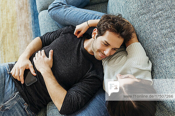 Smiling boyfriend looking at girlfriend while lying on sofa at home