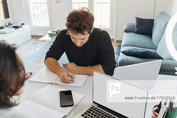 Young businessman writing in book while working at home office