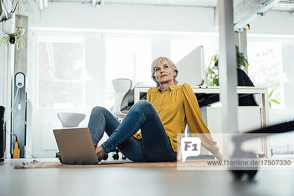 Thoughtful businesswoman with laptop relaxing at office