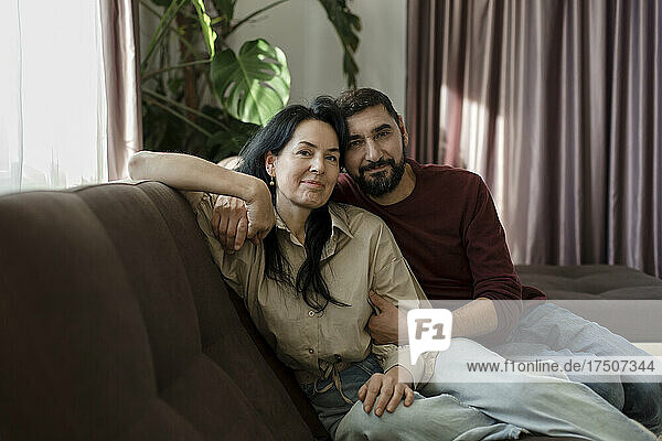 Smiling man embracing woman sitting on sofa in living room at home