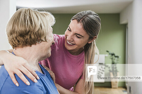 Young physiotherapist with hand on woman's shoulder at home
