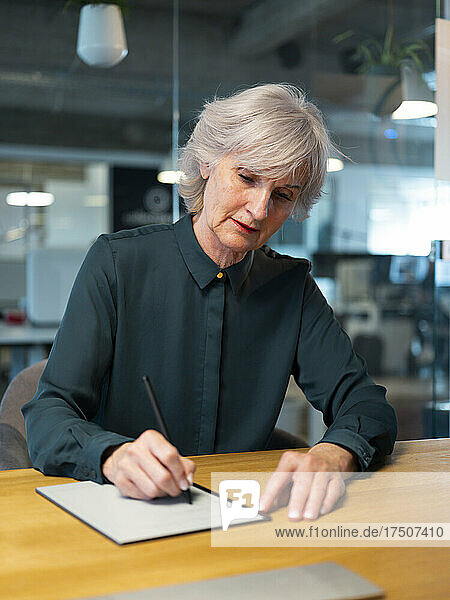 Ältere Geschäftsfrau schreibt am Schreibtisch auf Notizblock