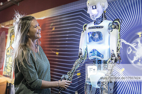 Happy technician shaking hands with human robot at workshop