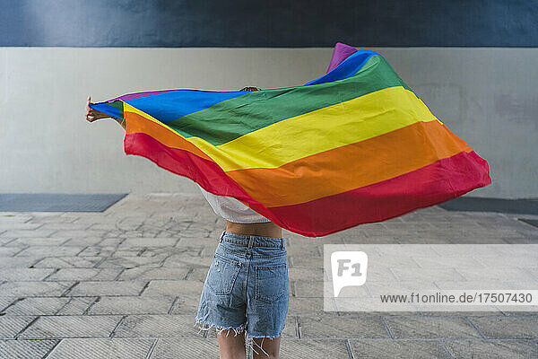 Woman with denim shorts holding rainbow flag on footpath