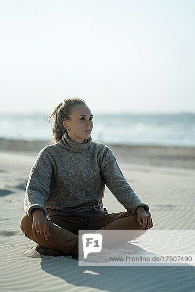 Junge Frau sitzt auf Sand am Strand